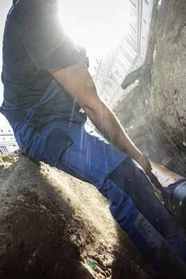 Ein Mann in einem blauen Arbeitsanzug platziert bei strahlendem Sonnenschein und blauem Himmel sorgfältig ein Rohr in einem vorbereiteten Baugraben.