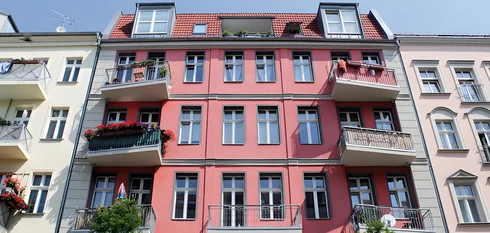 Mehrstöckiges Wohnhaus mit roten Fassaden und mehreren Balkonen, einige mit Pflanzen und Blumen geschmückt
