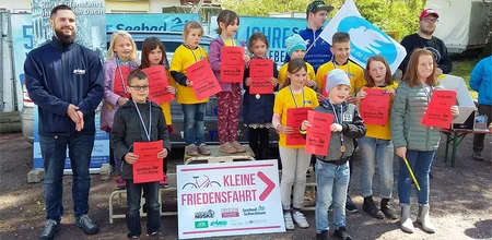 Kinder stehen mit Urkunden und Medaillen bei der Siegerehrung der Kleinen Friedensfahrt, begleitet von einigen Erwachsenen