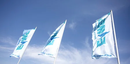 Drei weiße, von unten betrachtete, EMS-gebrandete Flaggen wehen im Wind bei blauem Himmel.