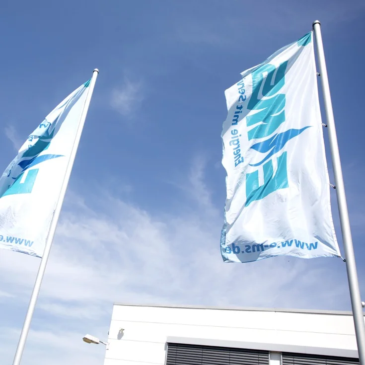 Drei weiße, von unten betrachtete, EMS-gebrandete Flaggen wehen im Wind bei blauem Himmel.