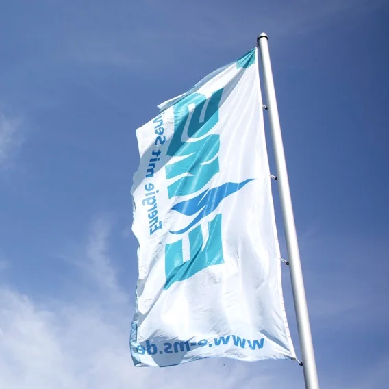 Drei weiße, von unten betrachtete, EMS-gebrandete Flaggen wehen im Wind bei blauem Himmel.