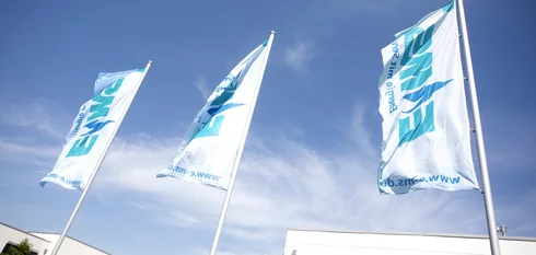 Drei weiße, von unten betrachtete, EMS-gebrandete Flaggen wehen im Wind bei blauem Himmel.