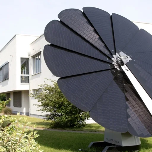Die aufgefahrene große E-Solarblume auf der Grünfläche, des großen weißen EMS-Gebäudes, bei blauem Himmel.