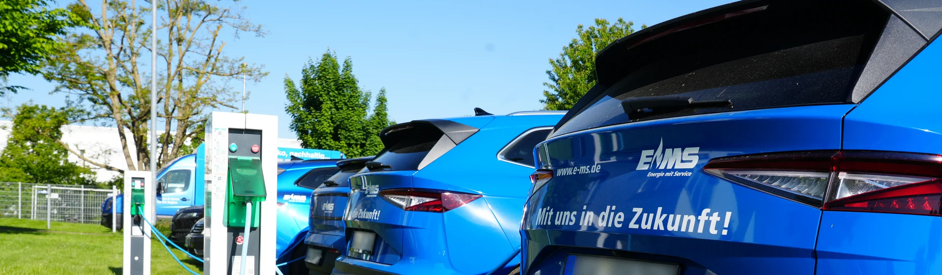 Mehrere elektrische EMS Firmenwagen stehen an einem sonnigen Tag mit dem Heck zu Ladesäulen und werden geladen