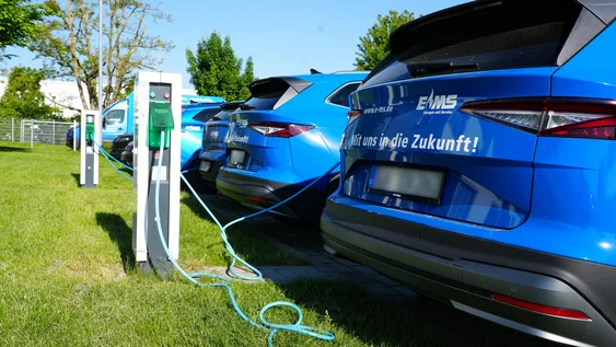 Mehrere elektrische EMS Firmenwagen stehen an einem sonnigen Tag mit dem Heck zu Ladesäulen und werden geladen