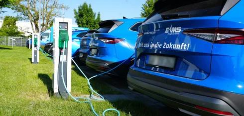 Mehrere elektrische EMS Firmenwagen stehen an einem sonnigen Tag mit dem Heck zu Ladesäulen und werden geladen