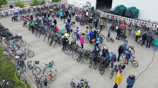 Aus der Vogelperspektive sieht man eine Gruppe von Fahrrädern, die ordentlich geordnet in einem abgesperrten Bereich auf dem Gelände der EMS stehen, während sich dazwischen Menschen mit Fahrradhelmen bewegen oder in kleinen Gruppen zusammenstehen und sich unterhalten.