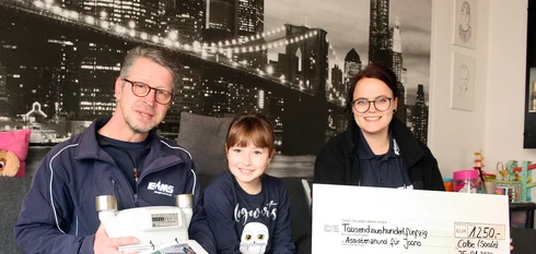 EMS Mitarbeiter überreichen einen Spendencheck für einen Assistenzhund einem Mädchen