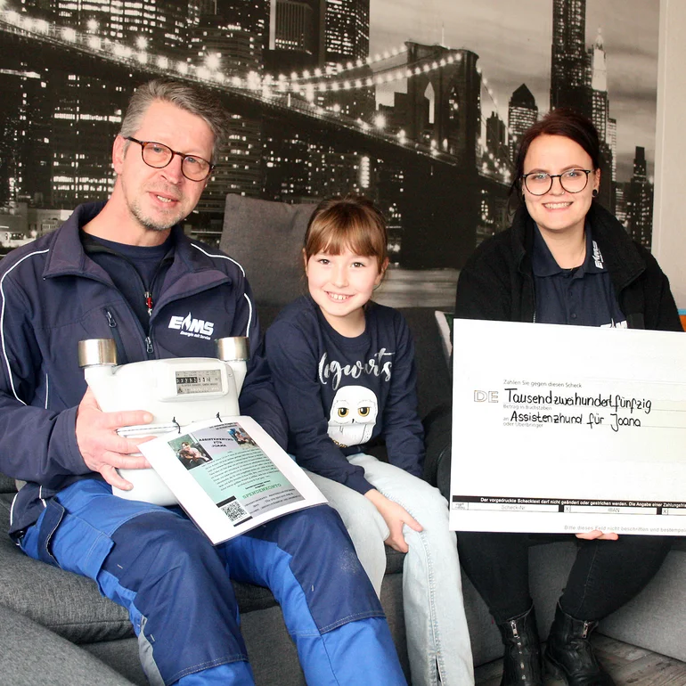 EMS Mitarbeiter überreichen einen Spendencheck für einen Assistenzhund einem Mädchen