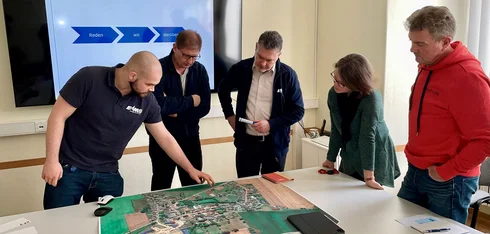 Fünf Mitarbeiter schauen in einem modernen Büroraum auf eine Karte, die auf einem Tisch liegt