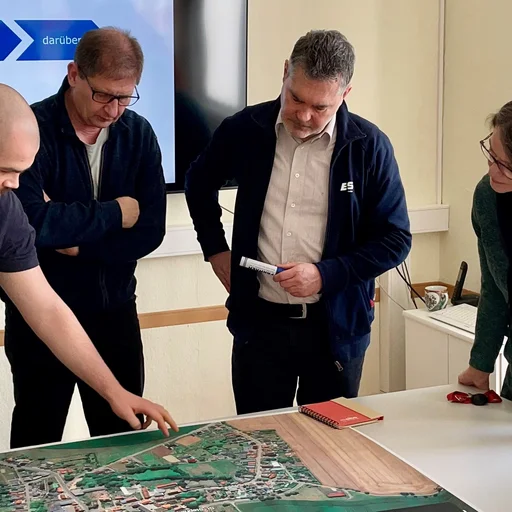 Fünf Mitarbeiter schauen in einem modernen Büroraum auf eine Karte, die auf einem Tisch liegt