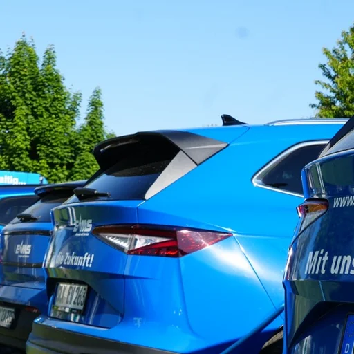 Mehrere elektrische EMS Firmenwagen stehen an einem sonnigen Tag mit dem Heck zu Ladesäulen und werden geladen